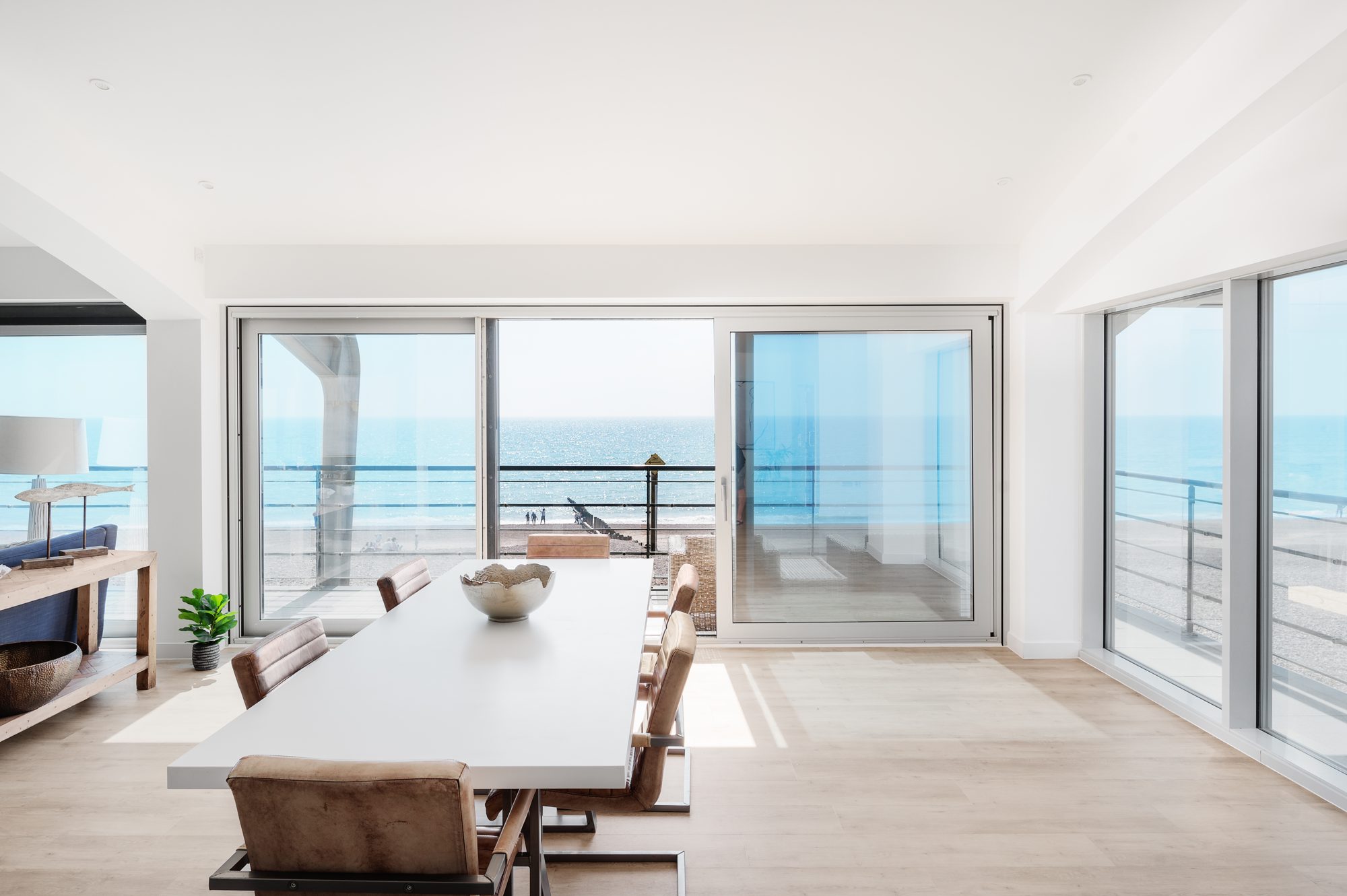 A dining table set by the windows of a seafront apartment, with the sea beyond